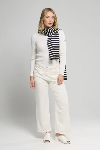 Woman in white sweater, wide-leg cream pants, and black and white striped scarf on plain background