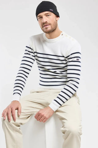 Man wearing a white Breton striped sweater, beige pants, and black beanie