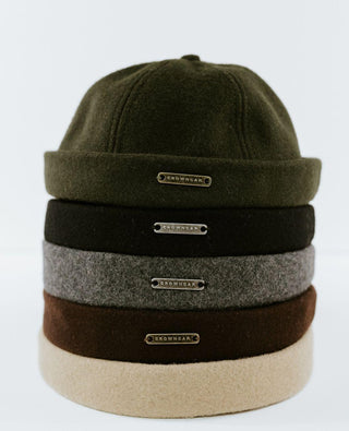 Stack of five wool beanies in green, black, grey, brown, and beige with metal tags