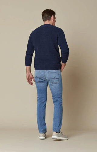 Man in blue ribbed sweater and light blue slim fit jeans standing against beige background