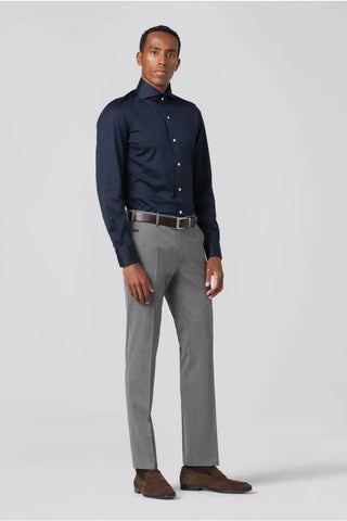Man wearing light grey wool dress pants, navy dress shirt, and brown loafers standing against a plain background