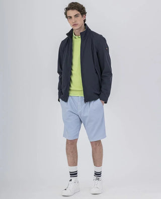 Man wearing navy nylon jacket, neon green sweater, light blue shorts, striped socks, white sneakers