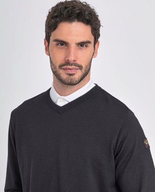 Man wearing black merino wool V-neck sweater over white shirt, close-up on neutral background